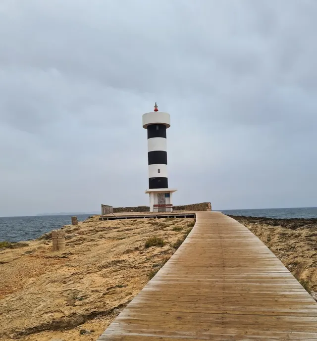 Ein schwarz-weiß gestreifter Leuchtturm am Meer, zu dem ein Holzsteg führt